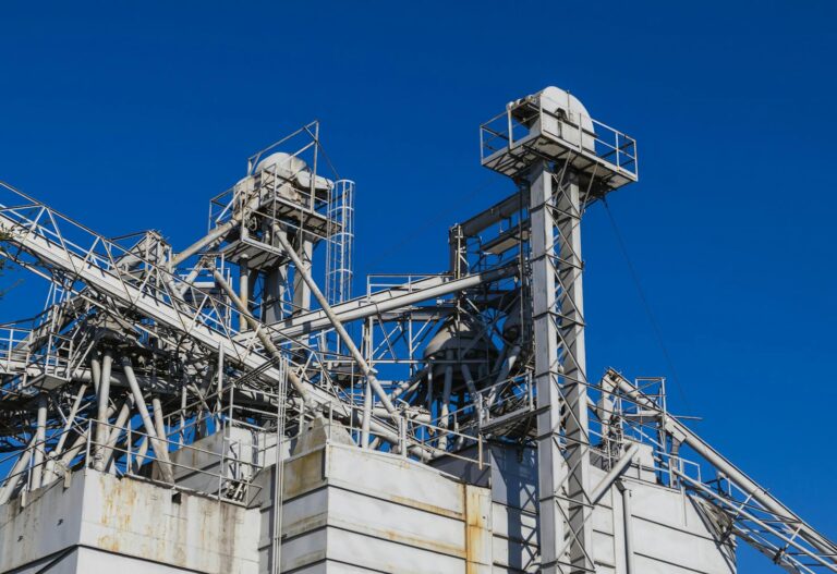 Detailed view of metal industrial structures with pipes and beams against a clear blue sky.