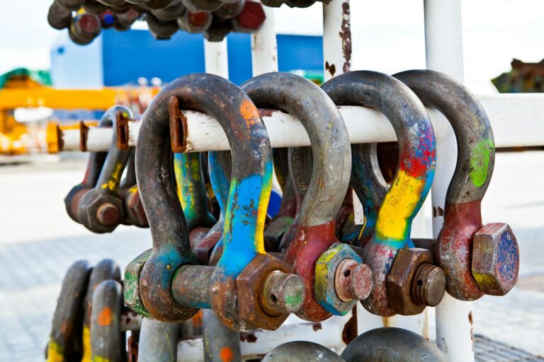 Close-up of colorful rusted shackles on a rack, showcasing industrial wear and vibrant paint.